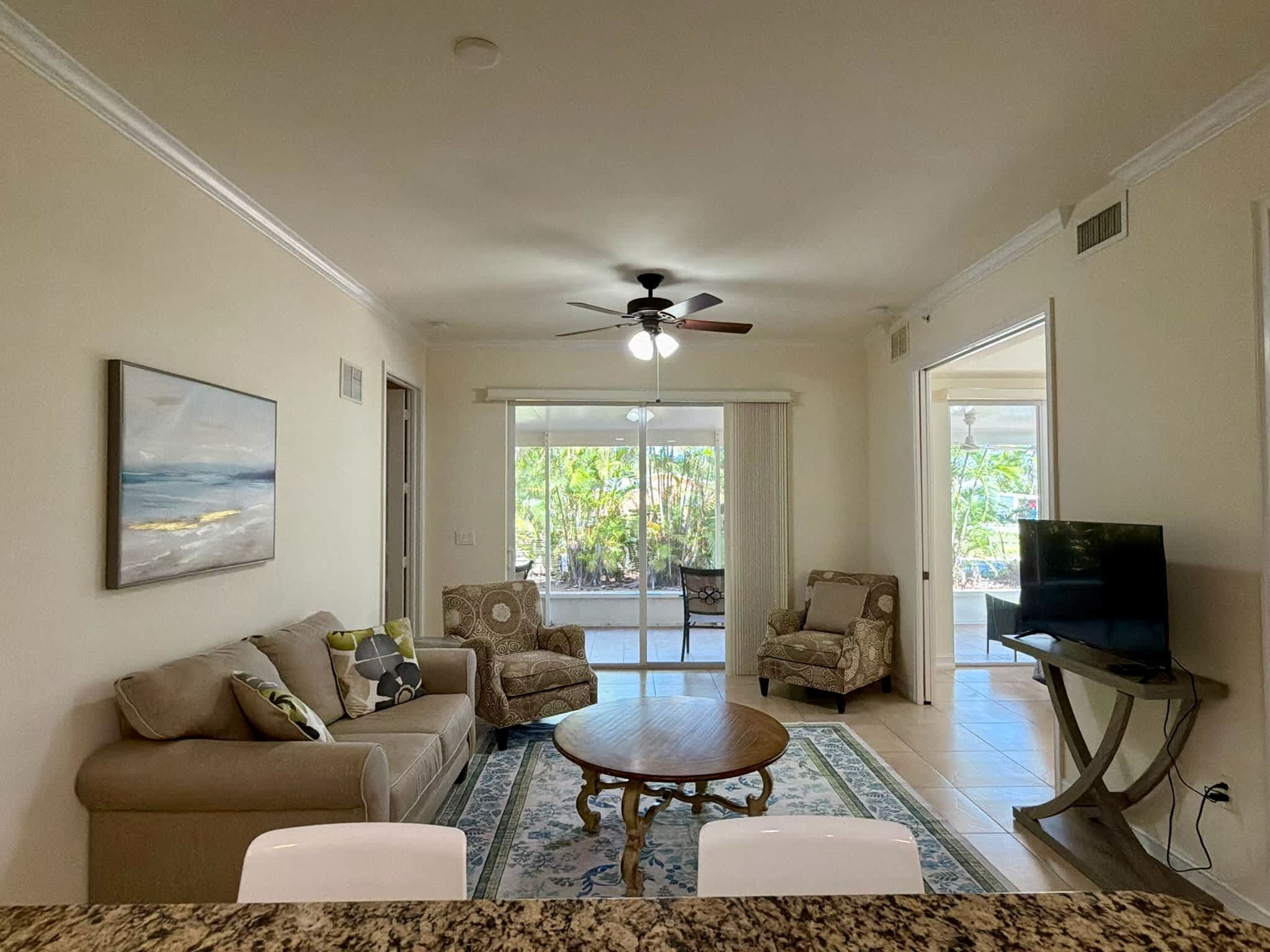 A living room with a sofa, armchairs, a coffee table, a television on a stand, and a ceiling fan.