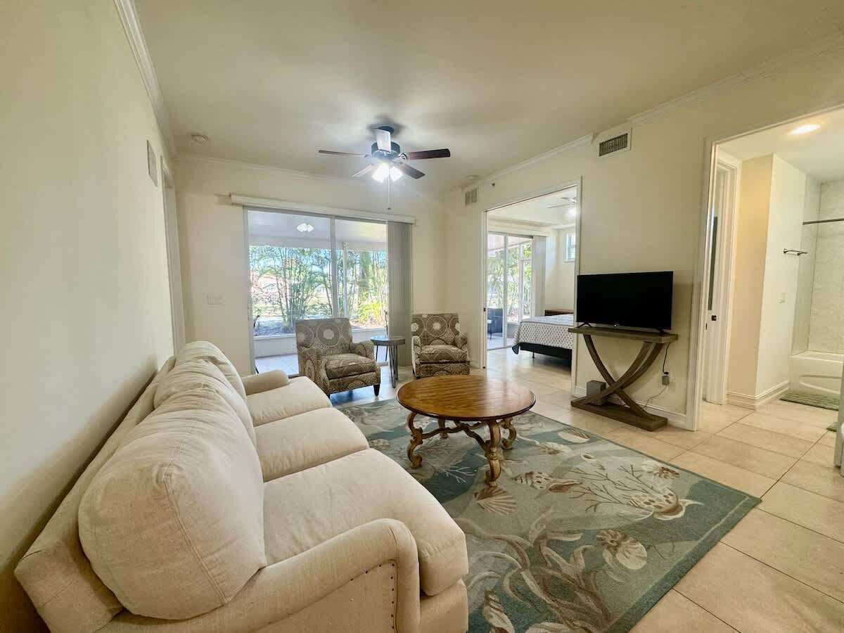 A living room with a beige sofa, a wooden coffee table, and a television on a stand. There are two armchairs and a patterned rug.