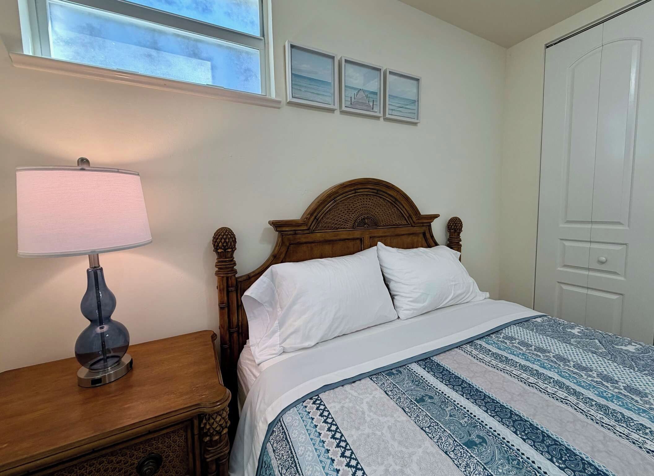 Un dormitorio con una cama de madera, una mesita de noche con lámpara y una colcha estampada.