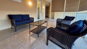 Un patio couvert aménagé avec des meubles en osier, une table basse en verre et un canapé bleu.