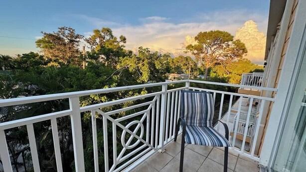 Un balcon avec une balustrade blanche, une chaise à rayures et une vue sur les arbres et les immeubles.