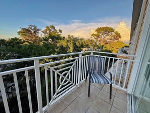 Un balcon avec une balustrade blanche, une chaise à rayures et une vue sur les arbres et les immeubles.