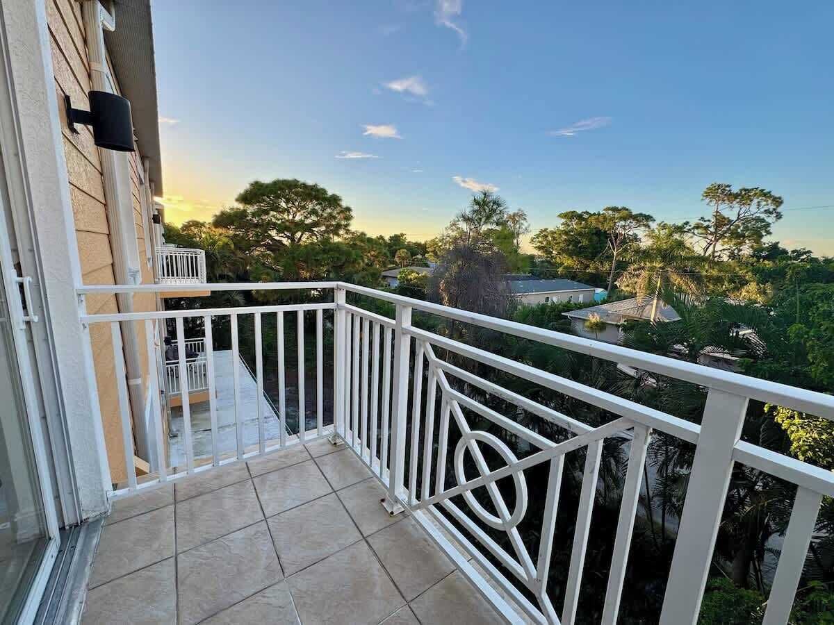 A balcony with white railings, a tiled floor, and a view of trees and houses in the background.