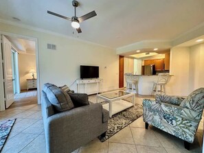 Ein Wohnzimmer mit einer Couch, einem gemusterten Sessel, einem Couchtisch, einem Fernseher und einem Deckenventilator.