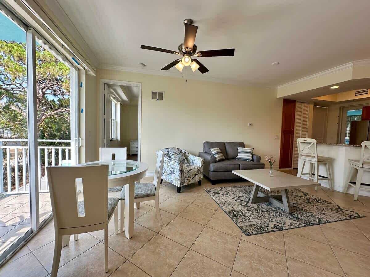A spacious living area with a ceiling fan, a dining table with chairs, a sofa, and a kitchen area in the background.
