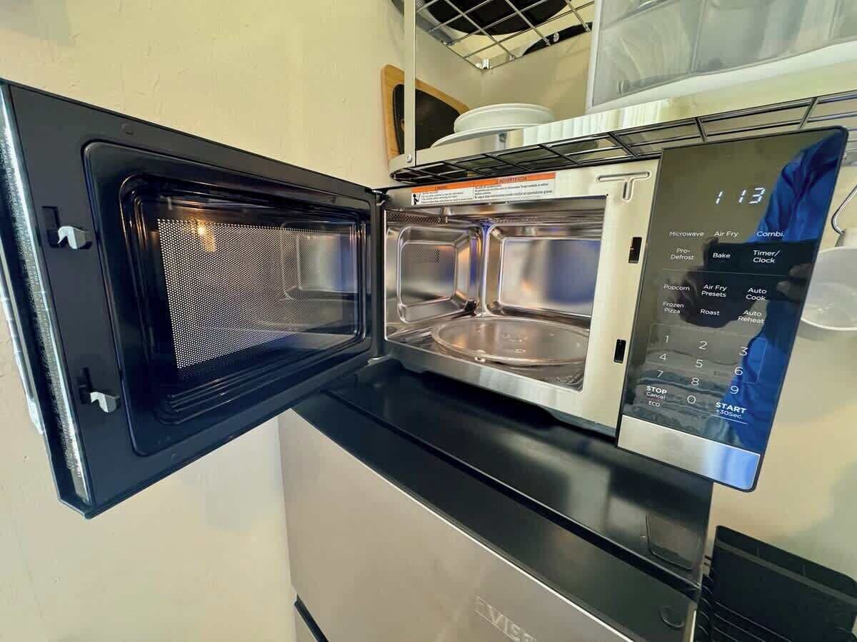 A kitchen with a microwave and oven, a digital control panel, and a microwave shelf above the oven.