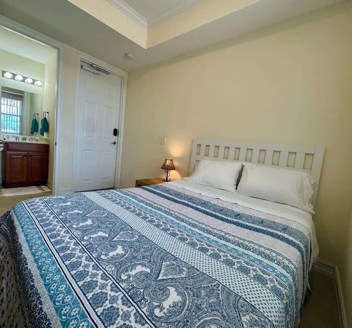Un dormitorio con una cama, una mesita de noche, una lámpara, un espejo y una puerta.
