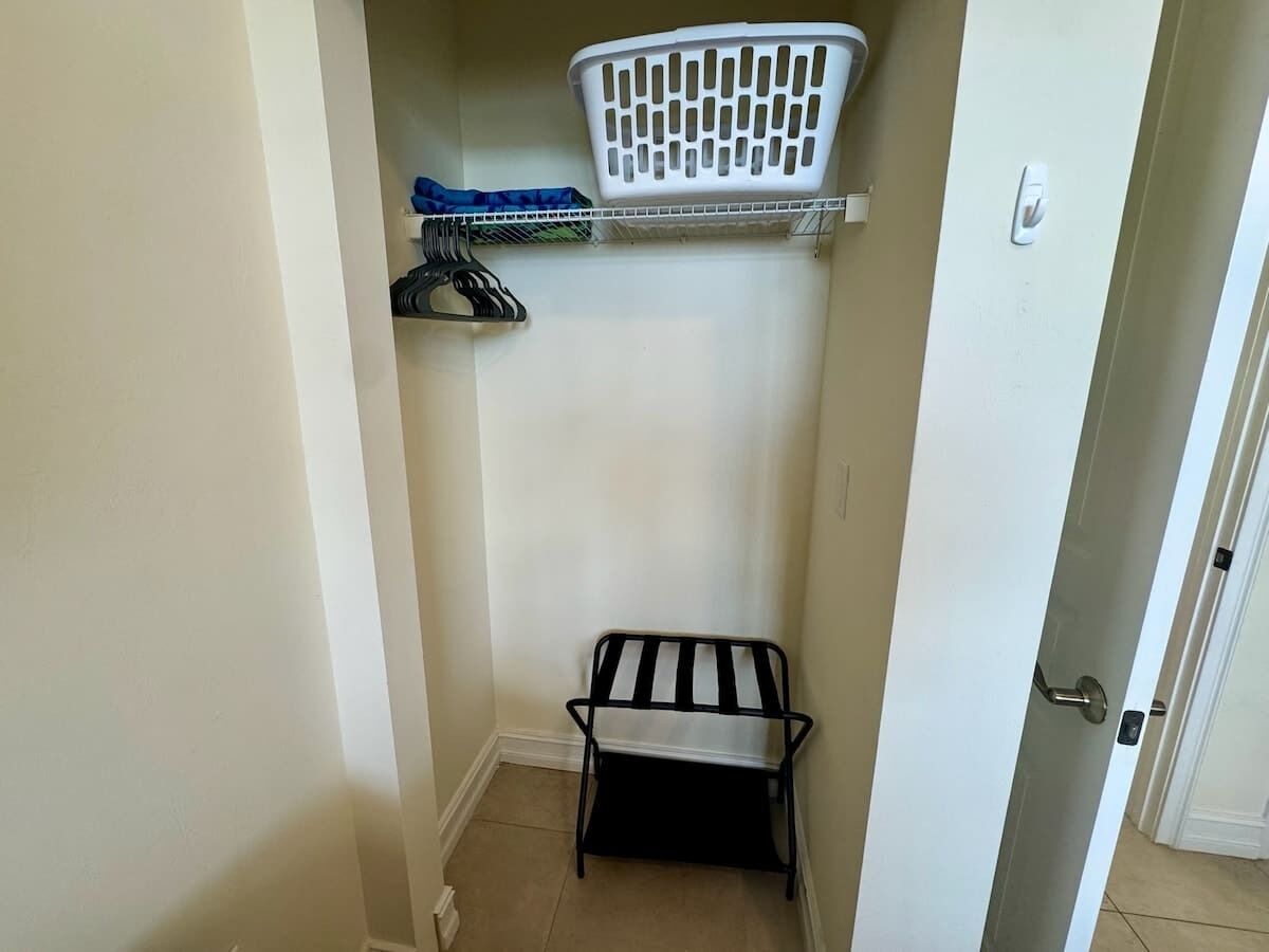 Een kleine berging met een metalen bankje, een witte wasmand en een plank met hangende kleding.