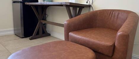 A brown leather armchair and ottoman in a room with a kitchenette area.