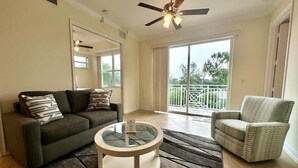 A living room with a sofa, armchair, and coffee table, a ceiling fan, and a view of the outdoors through a sliding glass door. - Sunlit Getaway – Free WiFi – 1 Mi to the Gulf (Bonita Springs)
