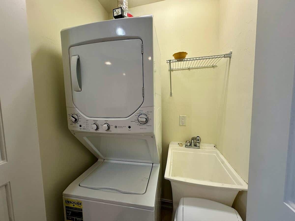 A compact laundry room with a front-loading washer and dryer, a small sink, and a shelf above the sink.
