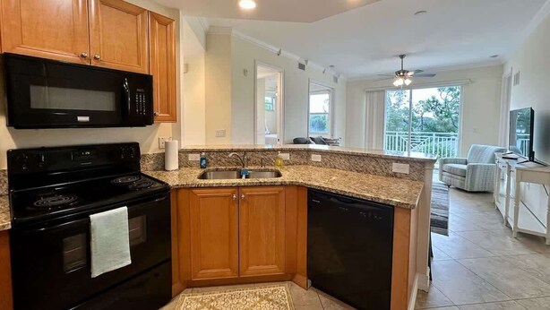 A modern kitchen with granite countertops, wooden cabinets, a black stove, and a dishwasher. - Sunlit Getaway – Free WiFi – 1 Mi to the Gulf (Bonita Springs)