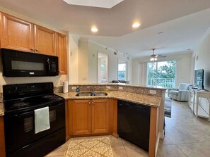 A modern kitchen with granite countertops, wooden cabinets, a black stove, and a dishwasher. - Sunlit Getaway – Free WiFi – 1 Mi to the Gulf (Bonita Springs)