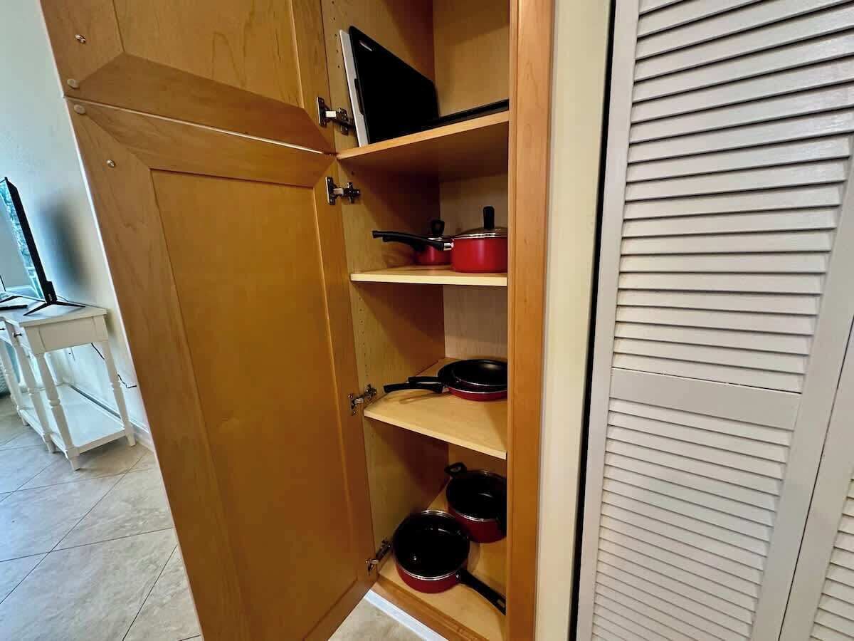 A wooden cabinet with shelves containing red pots and pans.