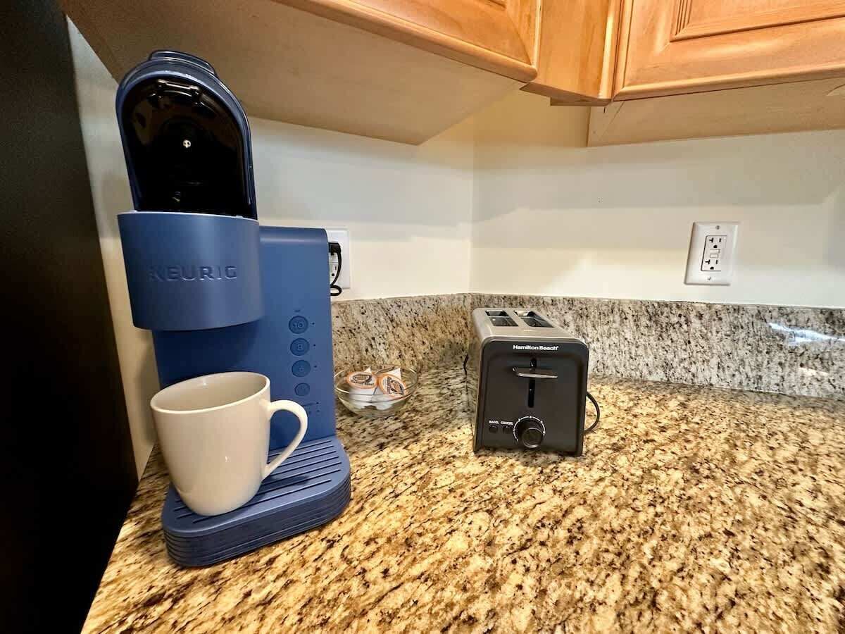 A kitchen with a Keurig coffee maker, a Hamilton Beach toaster, and a white mug on a granite countertop.