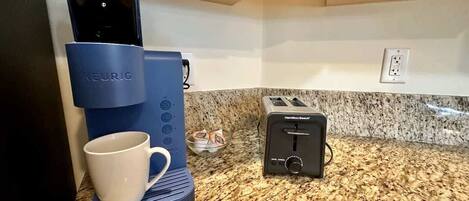 A kitchen with a Keurig coffee maker, a Hamilton Beach toaster, and a white mug on a granite countertop.
