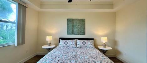 A bedroom with a bed, two bedside tables with lamps, a ceiling fan, and a window with curtains.