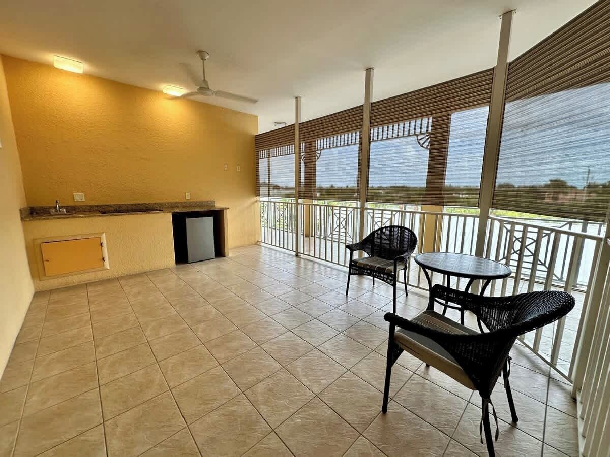 A spacious balcony with a kitchen area, including a sink and a small refrigerator. There are two black wicker chairs and a round table.