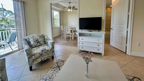 Un soggiorno con divano, mobile TV e tavolino. Include un balcone con una sedia e una ventola a soffitto.