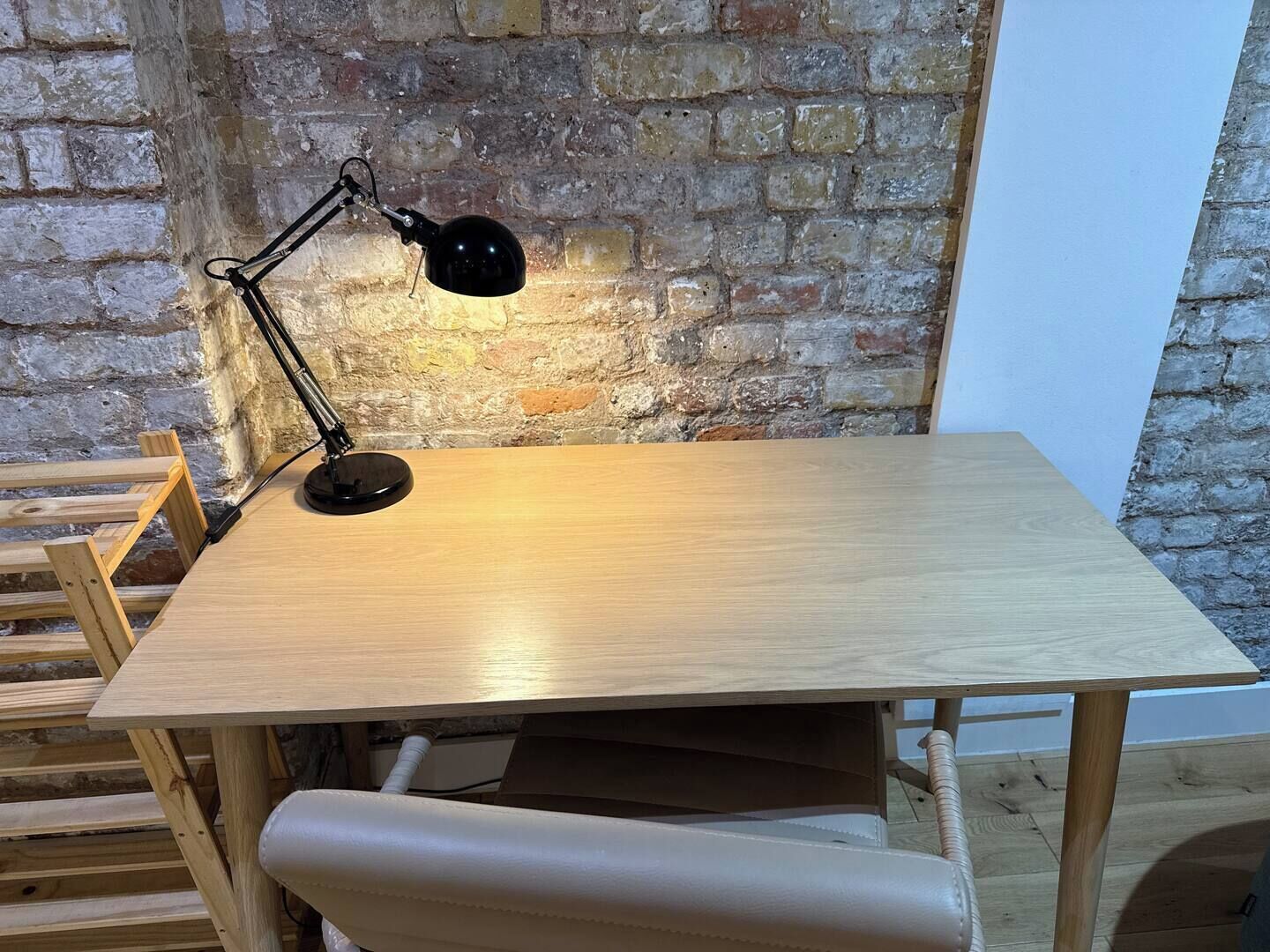 Ein Holztisch mit einer schwarzen Schreibtischlampe, vor einer Ziegelwand.