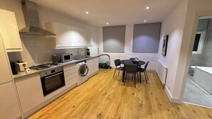 A compact kitchen with a gas stove, microwave, and washing machine, a dining area with a table and chairs, and a view of the adjacent bathroom. - Citylink Central Flat 1 (London)