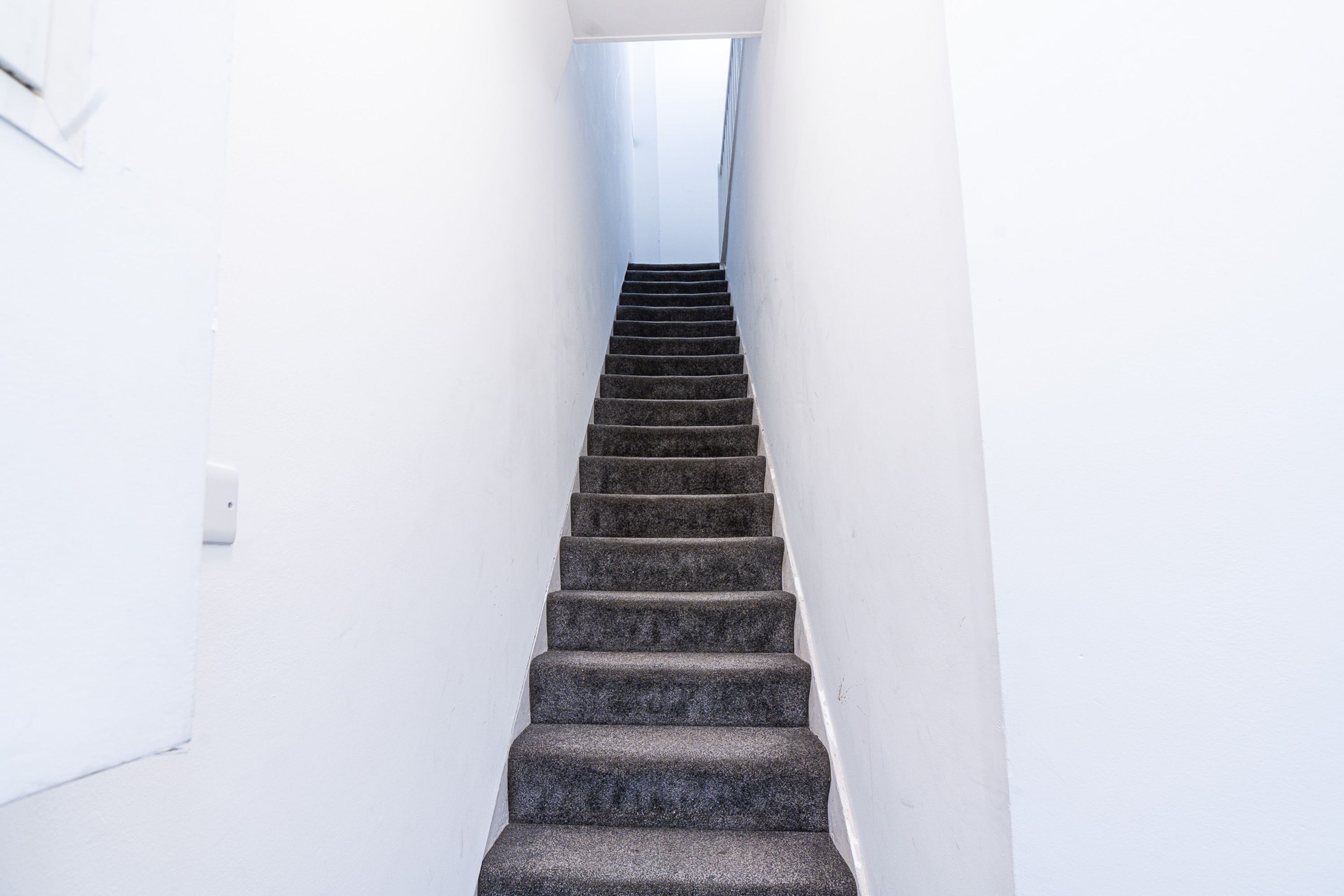 A staircase leading to a landing with a white wall on one side and a window at the top.