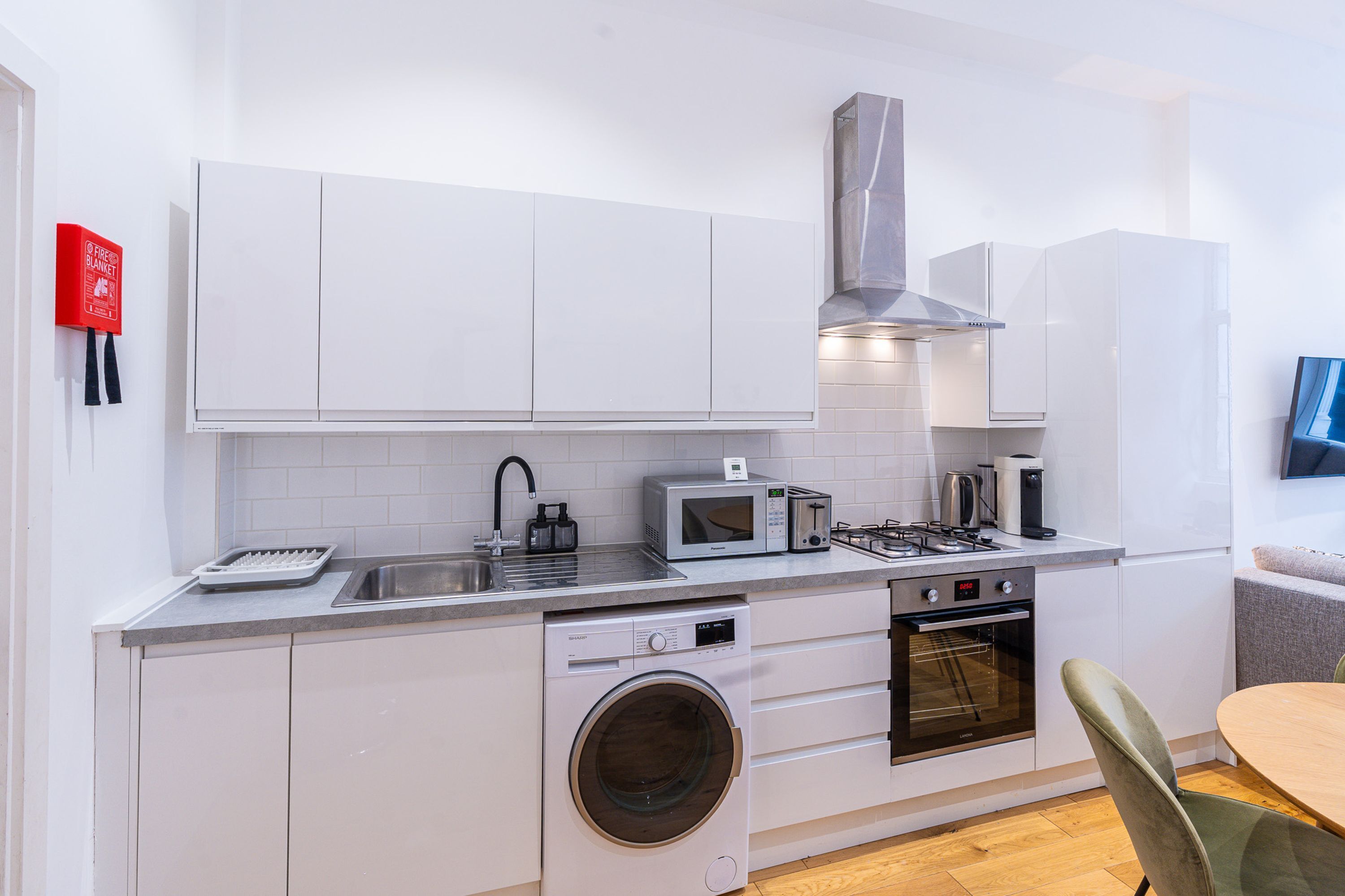 A modern kitchen with white cabinets, a stainless steel range hood, a microwave, toaster, and a built-in oven.