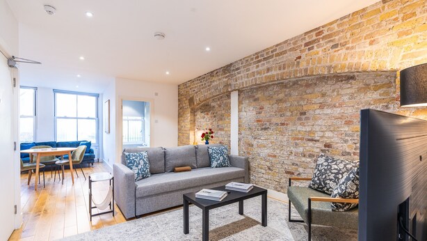 A modern living room with a brick wall, a grey sofa, a coffee table, and a television. - Citylink Central Flat 2 (London)
