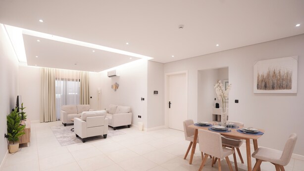 A modern living room with a sofa set, a dining table with chairs, and a kitchen area visible through an open door. - 2-bedroom apartment in beautiful Riyadh with Full Facilities (Riyadh)