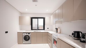 A modern kitchen with a built-in washer, oven, and a large window with blinds. - 2-bedroom apartment in beautiful Riyadh with Full Facilities (Riyadh)