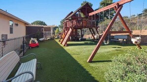 Un jardin avec une pelouse artificielle, une balançoire, une cabane et un banc.