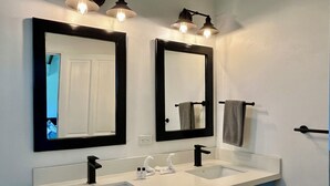 Casa de banho com duas pias, espelhos com moldura preta e um porta-toalhas.