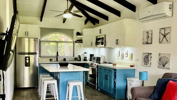 Uma cozinha moderna com armários brancos, uma ilha central e um espaço de refeições com um sofá e mesa de centro.