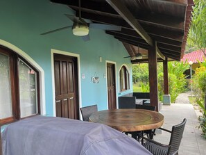 A covered outdoor seating area with a round table and chairs, a ceiling fan, and a view of a garden. - Comfy house in Potrero, next to pool, 2 bed/ 2 bath, close to town and beaches! (Potrero)