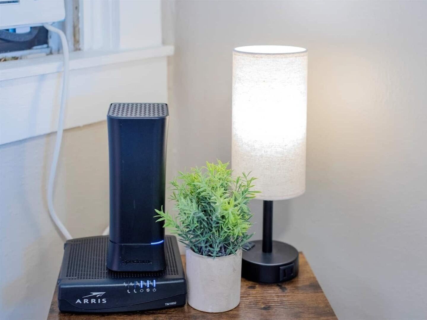 A black ARRIS Spectrum device on a wooden surface, a white lamp, and a small potted plant.
