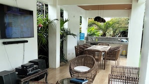 A modern living room with a flat-screen TV, audio system, wicker furniture, and a view of the outdoors.