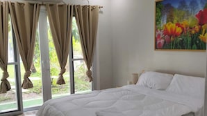 A bedroom with a large bed, beige curtains, a painting of flowers, and an air conditioning unit.
