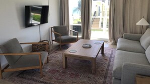 A living room with a flat-screen TV, a sofa, a chair, a coffee table, and a lamp. - Sub tropical paradise (Hillsboro Beach)