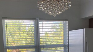 A dining area with a round wooden table, four chairs, a chandelier, and large windows with blinds. - Sub tropical paradise (Hillsboro Beach)
