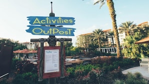 A signpost with 'Activities OutPost' written on it, surrounded by palm trees and a building in the background. - Unforgettable Family Fun Awaits at Holiday Inn Club Vacations Orange Lake- 2 Bd (Kissimmee)