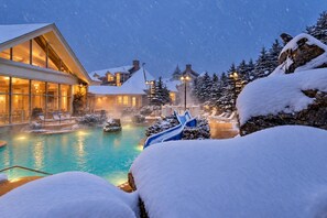 A resort with a heated pool, lounge chairs, and snow-covered trees.