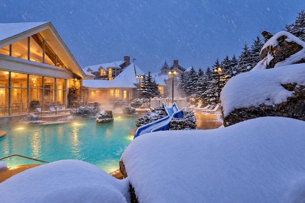 Un resort con piscina climatizada, sillas de descanso y árboles cubiertos de nieve.