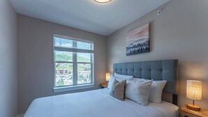Une chambre avec un grand lit, une fenêtre donnant sur des immeubles, un tableau accroché au mur et une lampe de chevet.
