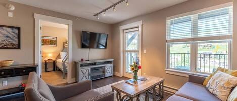 A modern living room with a sofa, armchairs, a coffee table, a TV, and a dining area with a table and chairs.