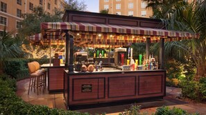Um bar tiki com toldo listrado, balcão e banquetes.