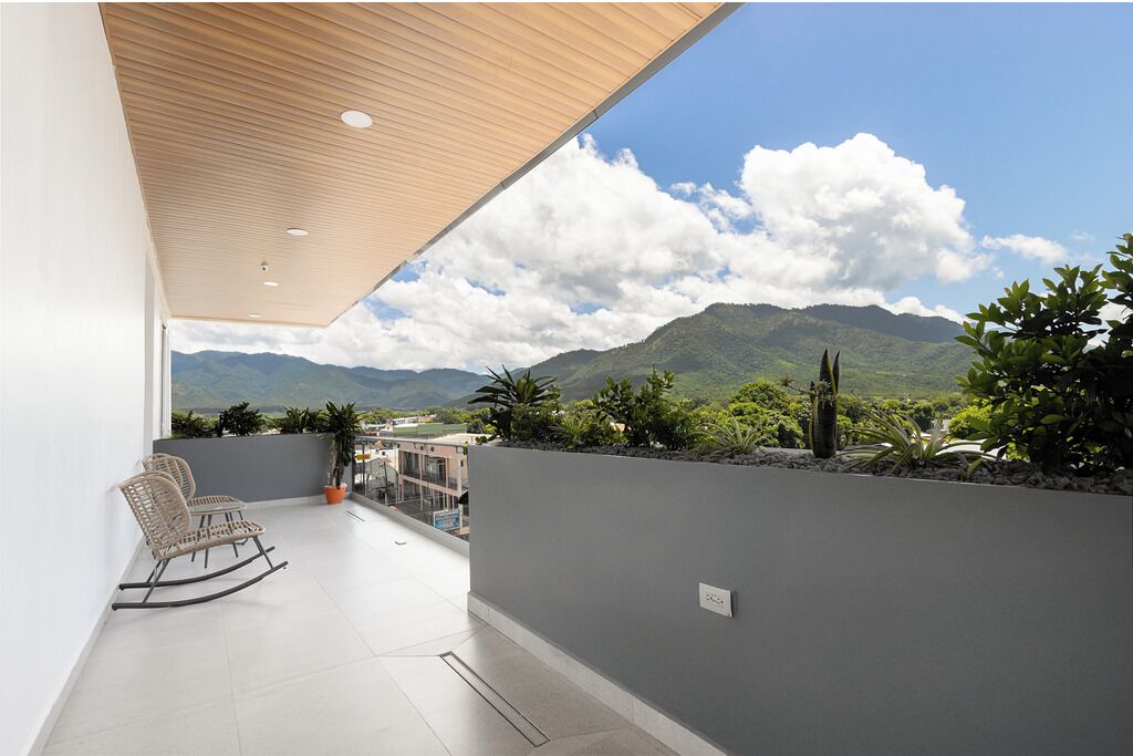 A balcony with a view of mountains, a wooden ceiling, and a seating area with chairs.