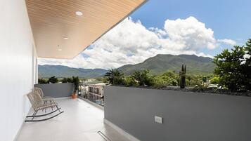 A balcony with a view of mountains, a wooden ceiling, and a seating area with chairs.