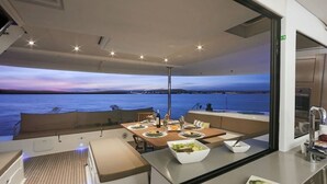 Un espace repas moderne avec vue sur la mer, une table dressée avec des assiettes et des verres, et un coin cuisine équipé d’un évier et d’une cuisinière.