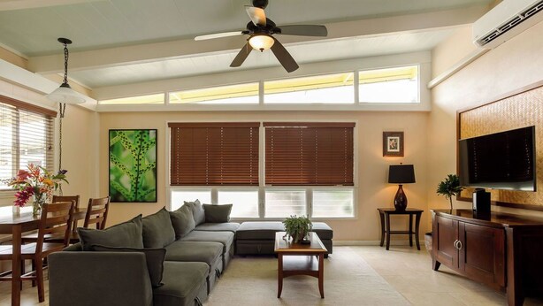 A spacious living room with a sectional sofa, a coffee table, a TV, and a ceiling fan.