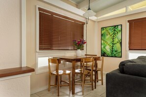 A dining area with a wooden table and chairs, a vase with flowers, and a painting on the wall.